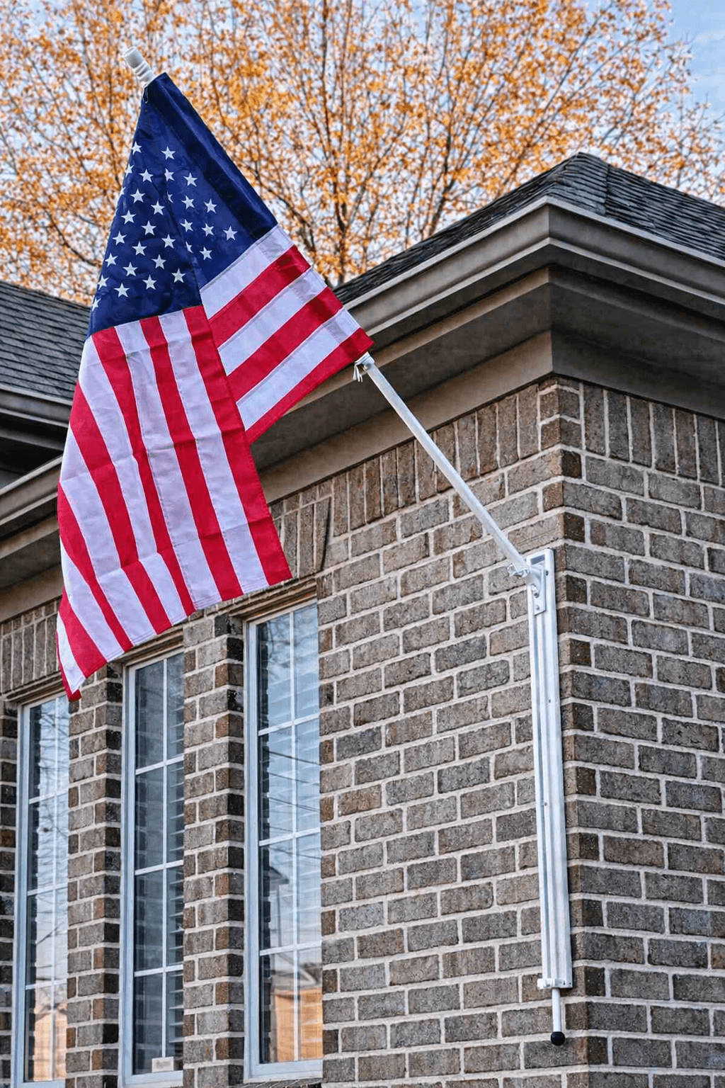 White VersaMAST flag mount raising an American flag on a brick home without a ladder